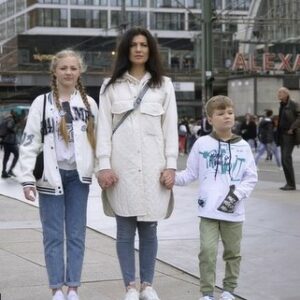 A woman holding a girl and a boy at her hands, standing on Alexanderplatz in Berlin, Germany